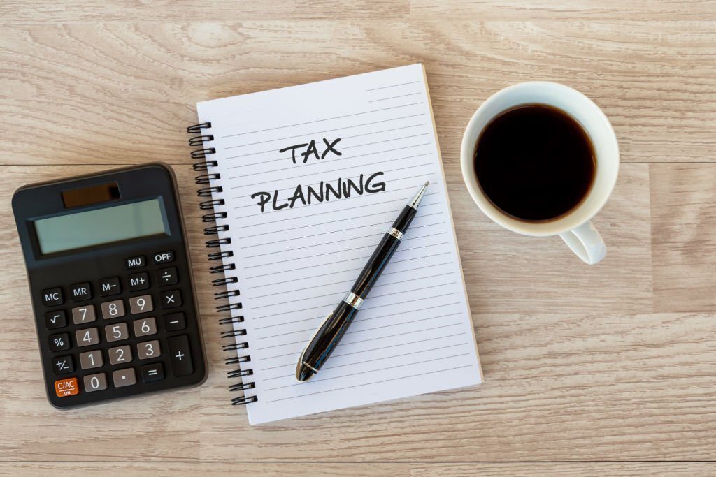 A pen, calculator and cup of coffee on top of a notebook.