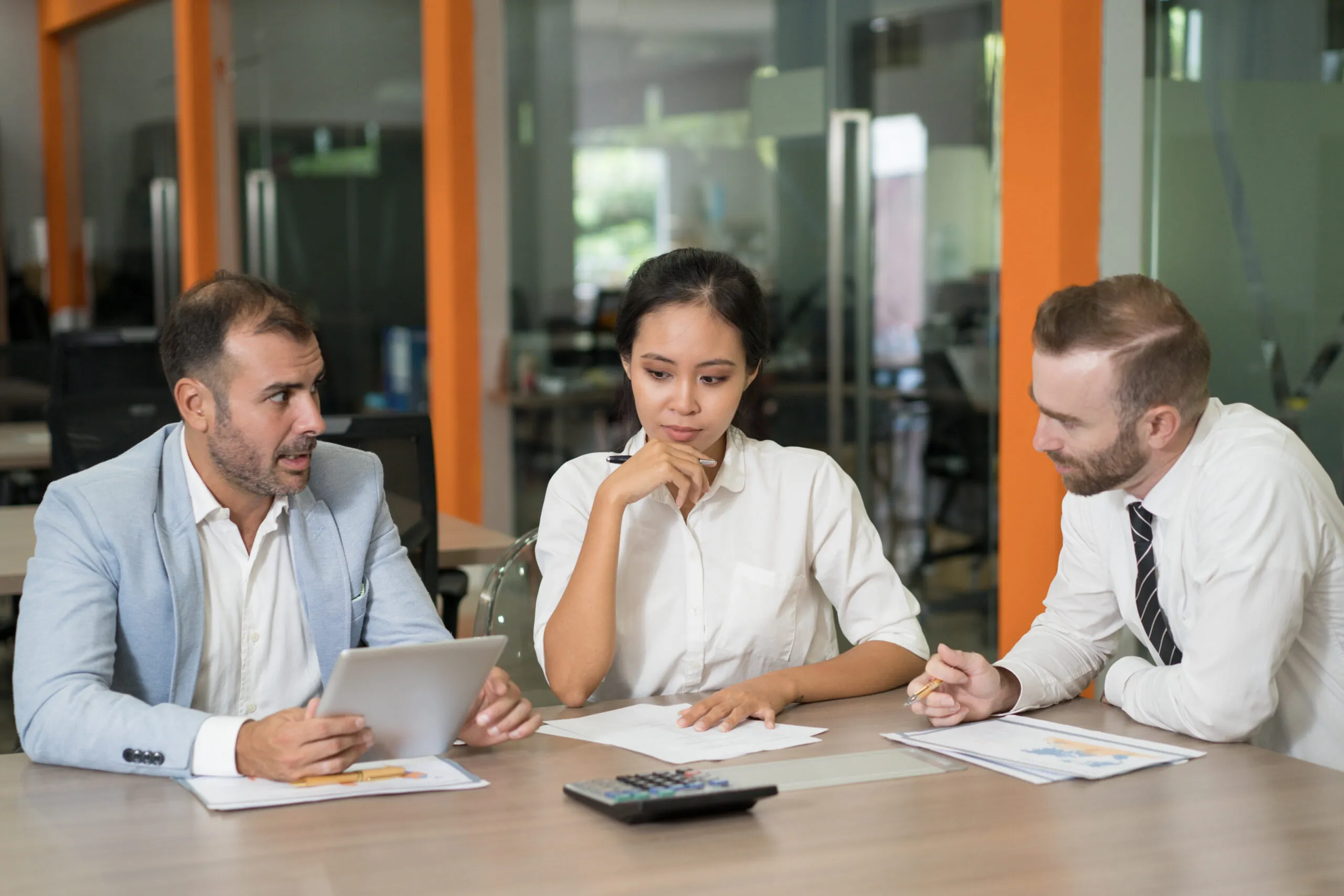 Stock photo of three business colleagues reviewing papers, a tablet and a calculator at an office table